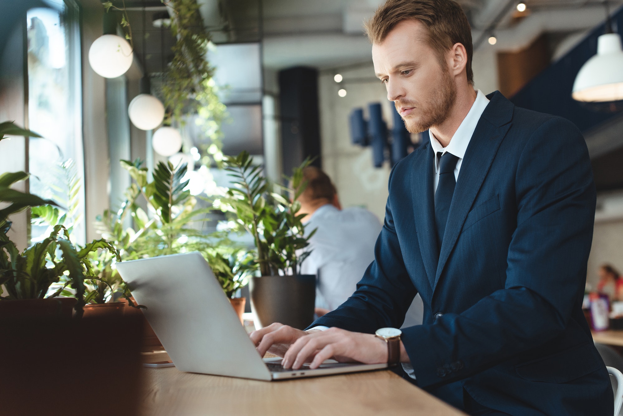 side view of focused businessman using laptop at table in cafe